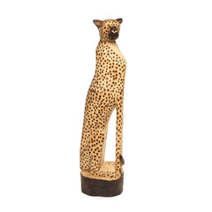 A statue of a sitting cheetah made of wood staring at the camera